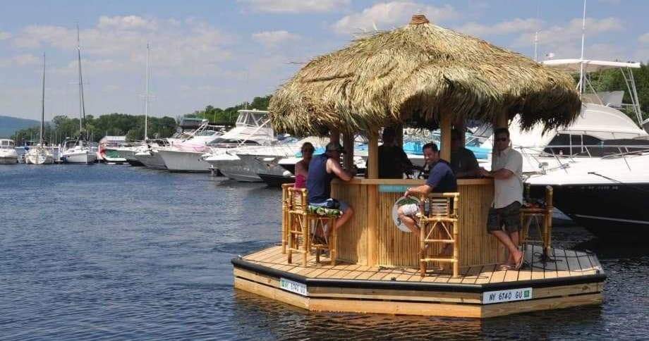 Floating tiki bar near marina with yachts on sunny day