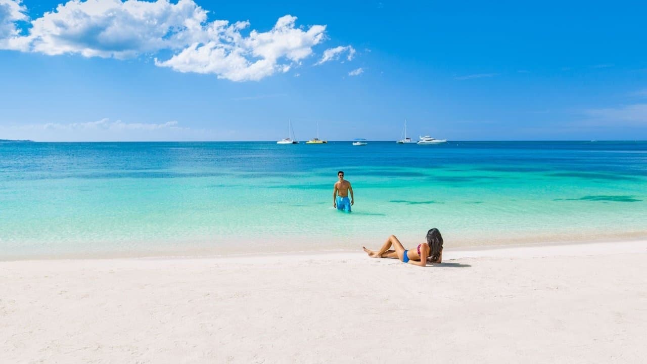 Couple relaxing on pristine white sand beach under blue sky