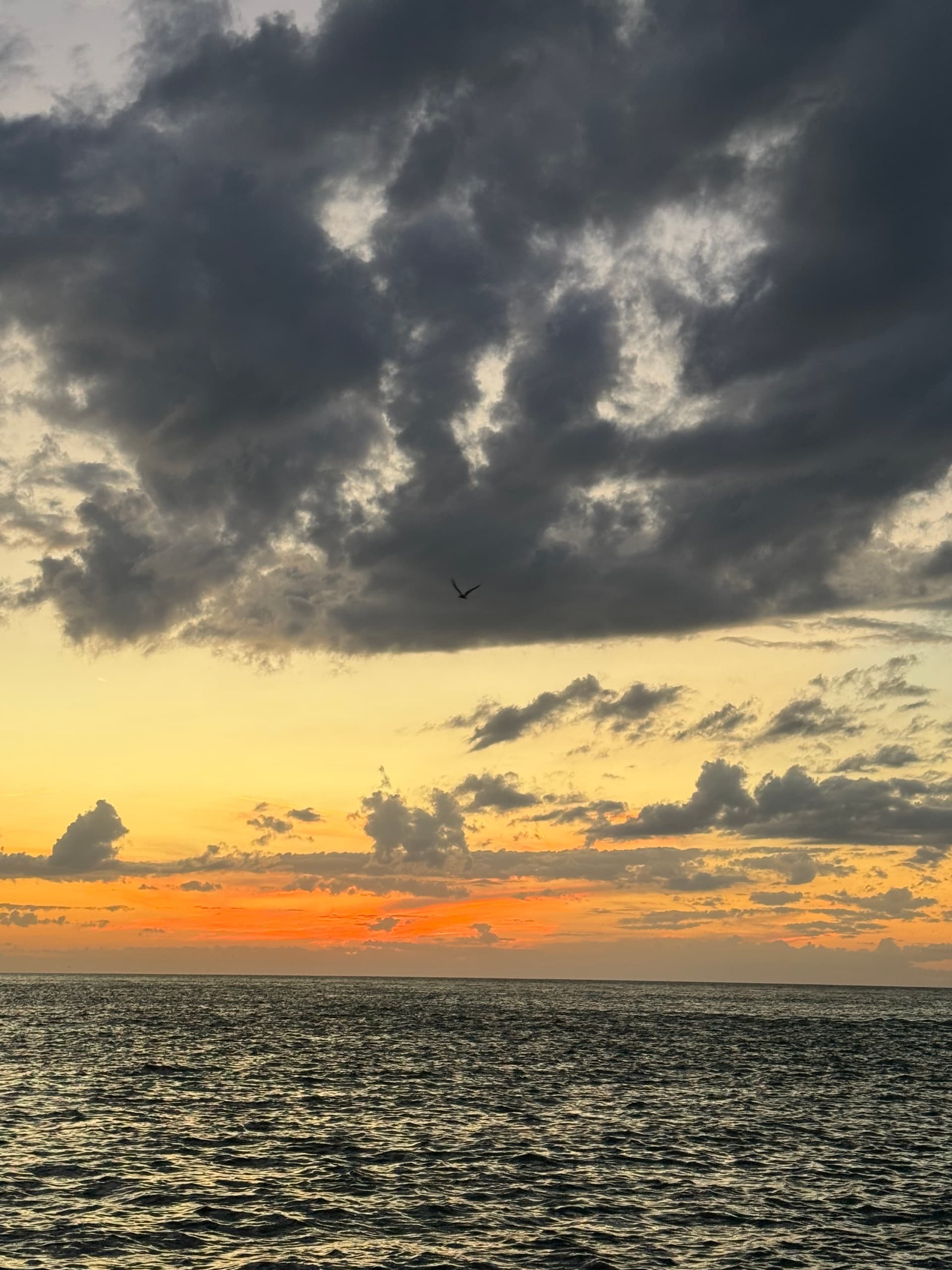 Dramatic cloud-streaked sunset over calm sea, scenic horizon view