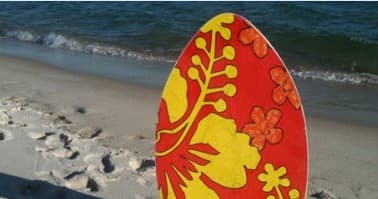 Hibiscus-patterned skimboard planted on sandy ocean beach