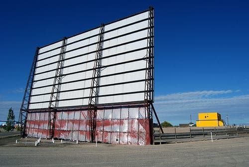 Outdoor drive-in movie screen at roadside under clear blue sky