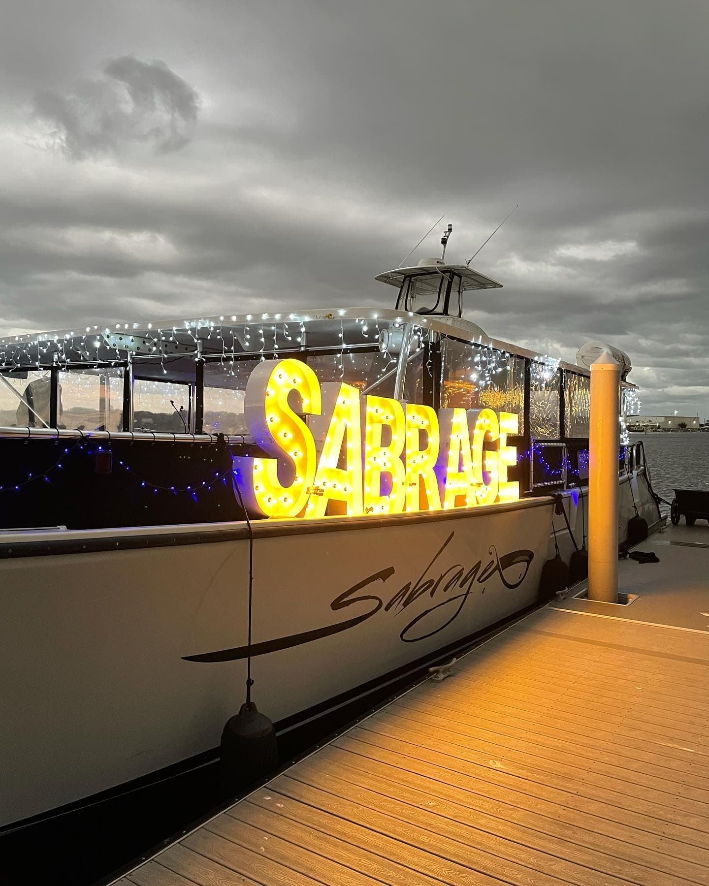 Docked party boat lit at night with Sabrage sign on marina pier