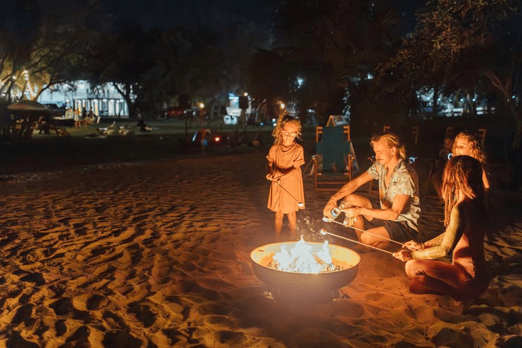Friends gathered around nighttime beach bonfire on sand