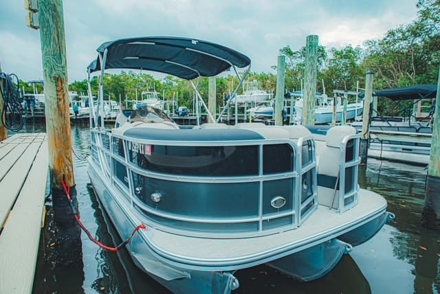 Pontoon boat docked at marina with calm water reflections