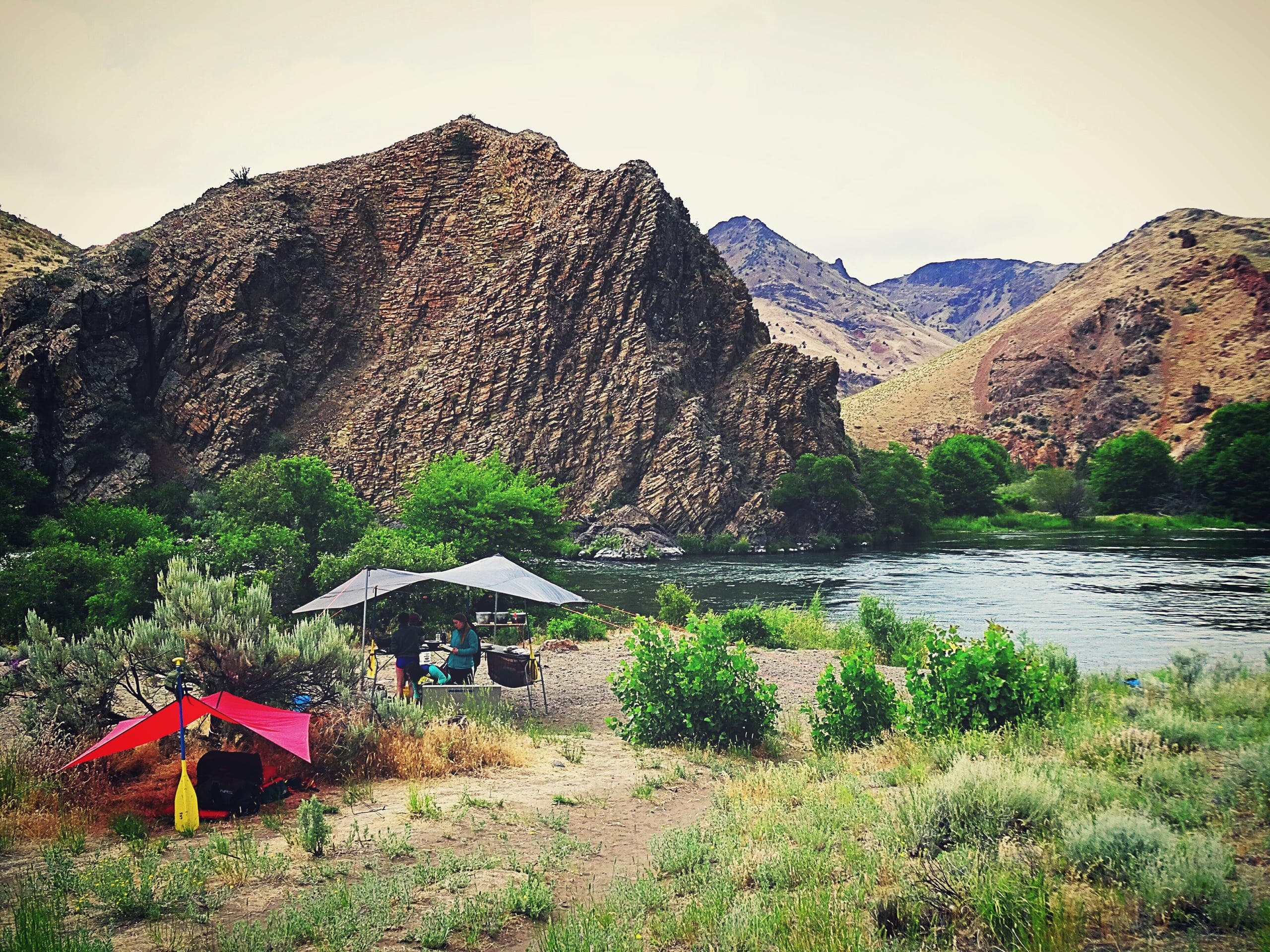 Riverside campsite with colorful tents and mountain vista