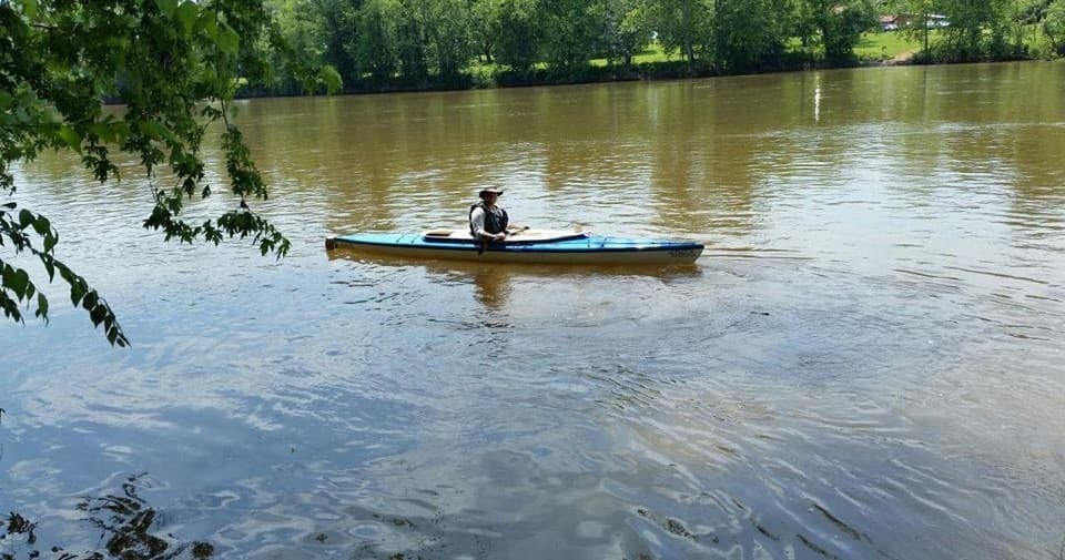 Solo kayaker paddling across tranquil tree-lined river
