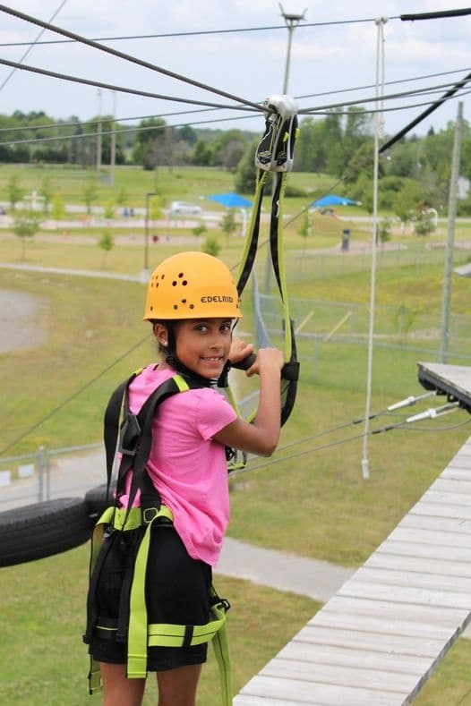 Teen on outdoor zipline platform wearing helmet and harness