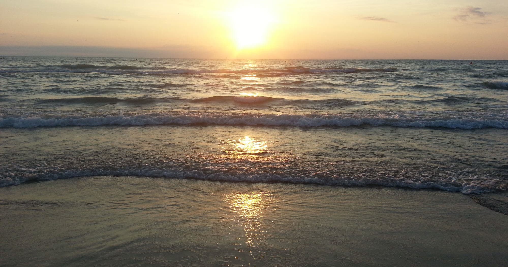 Sunset over ocean shoreline with calm waves, serene beachscape