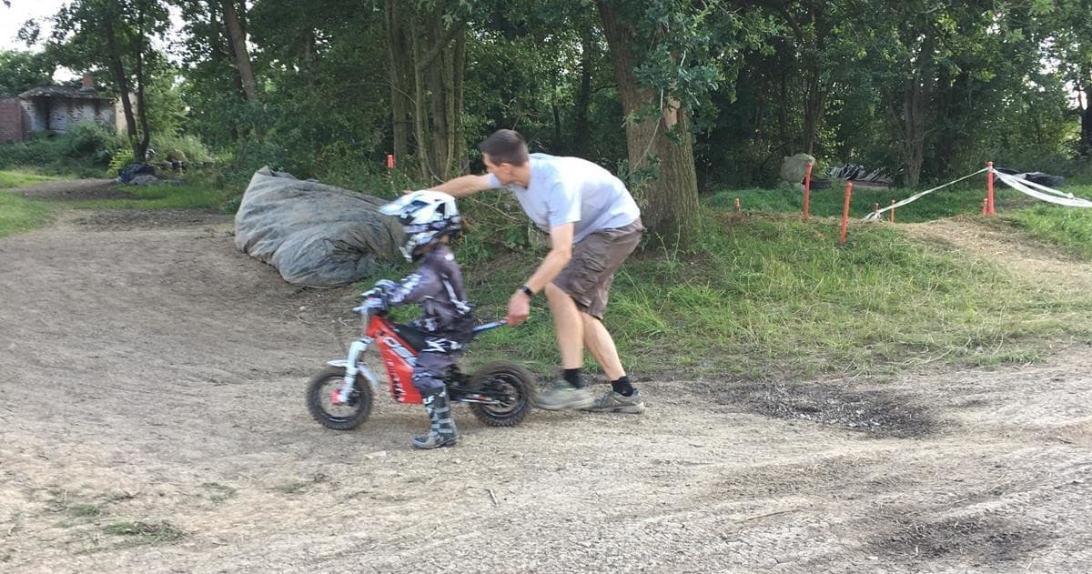 Parent coaching child on mini dirt bike at outdoor track