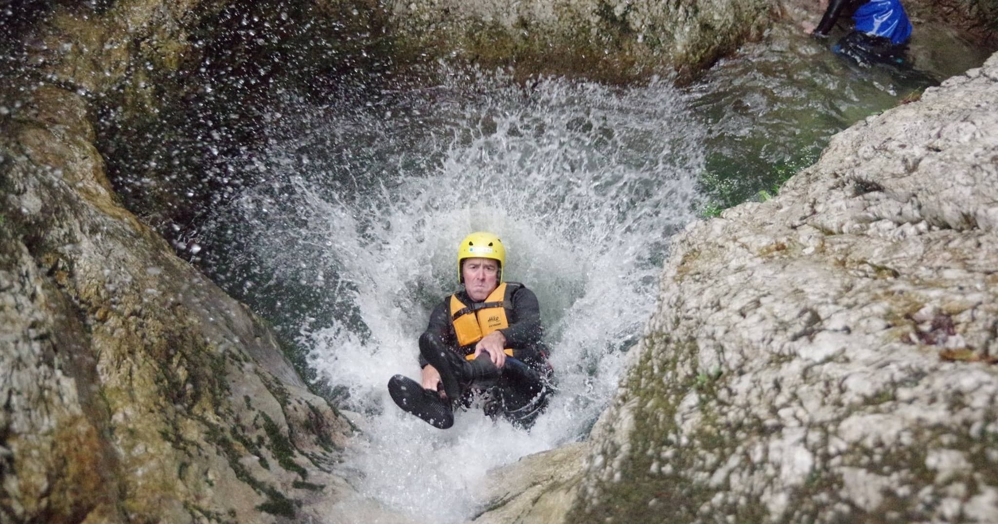 Canyoneer sliding into plunge pool amid steep rocky gorge waterfalls