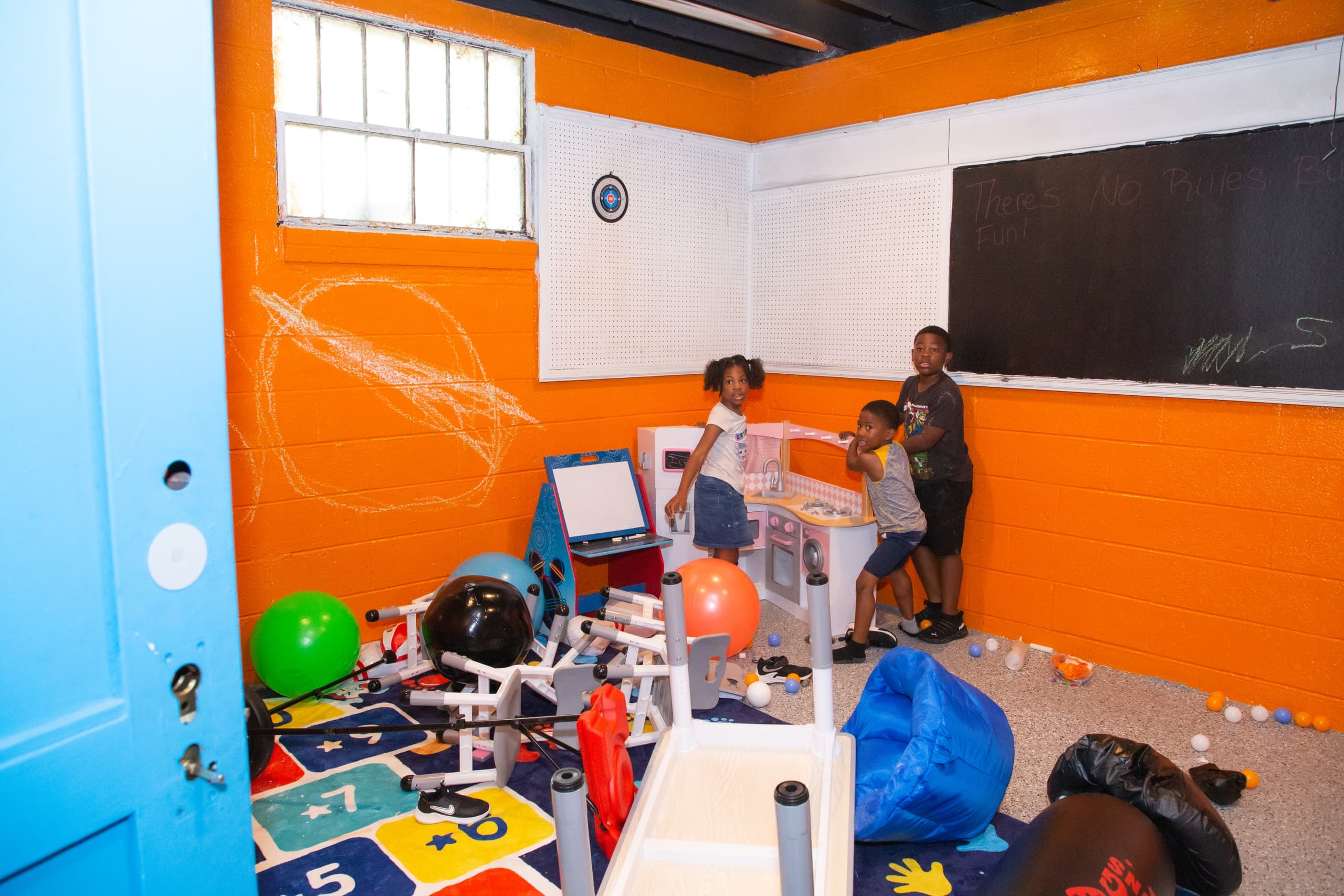 Children and staff in colorful indoor play/smash room with toys scattered