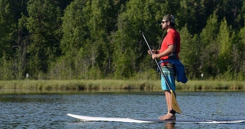 Man stand-up paddleboarding along forest-lined lake shore