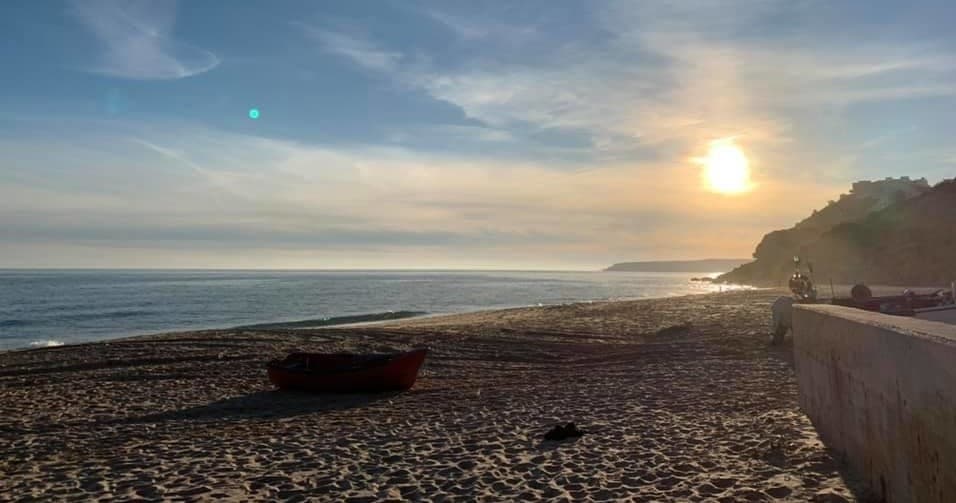 Sunset on sandy beach with small boat and coastal bluff