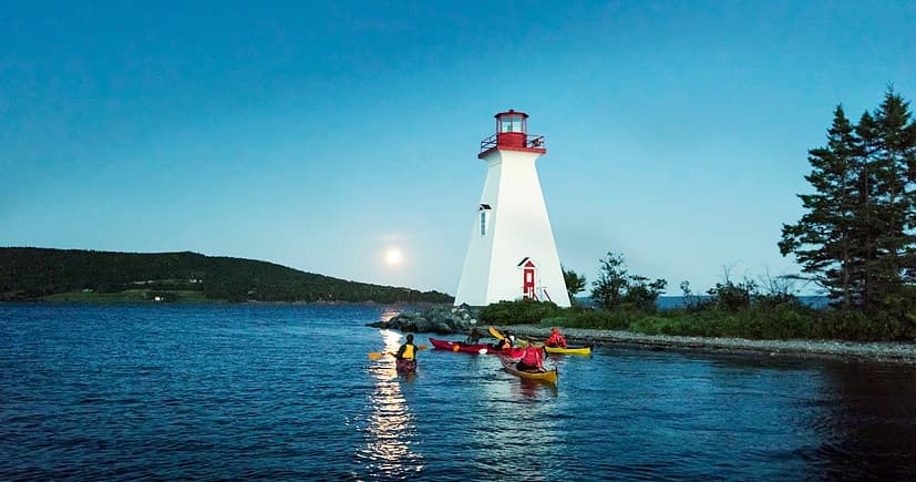 Kayakers paddling by white lighthouse at dusk on coastal bay