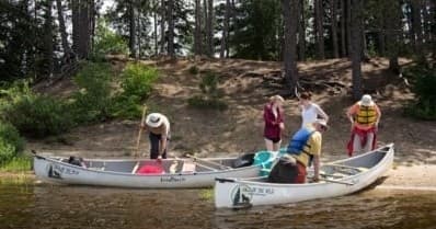 Group landing canoes on sandy forested shore during paddling trip