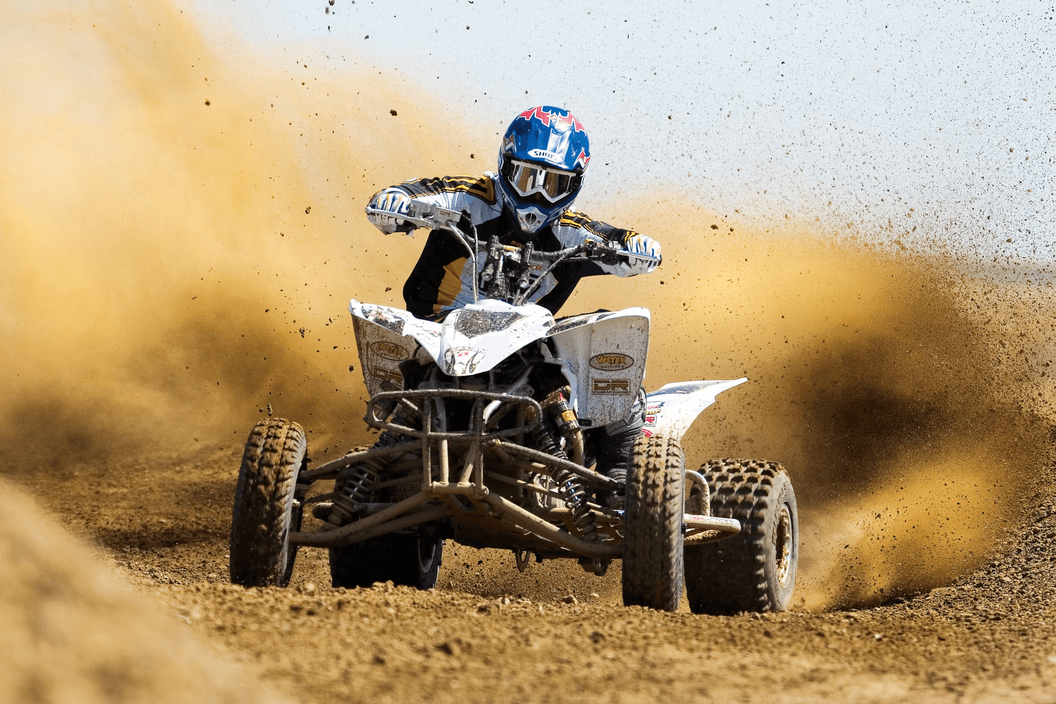 Rider racing an ATV kicking up dirt on desert trail