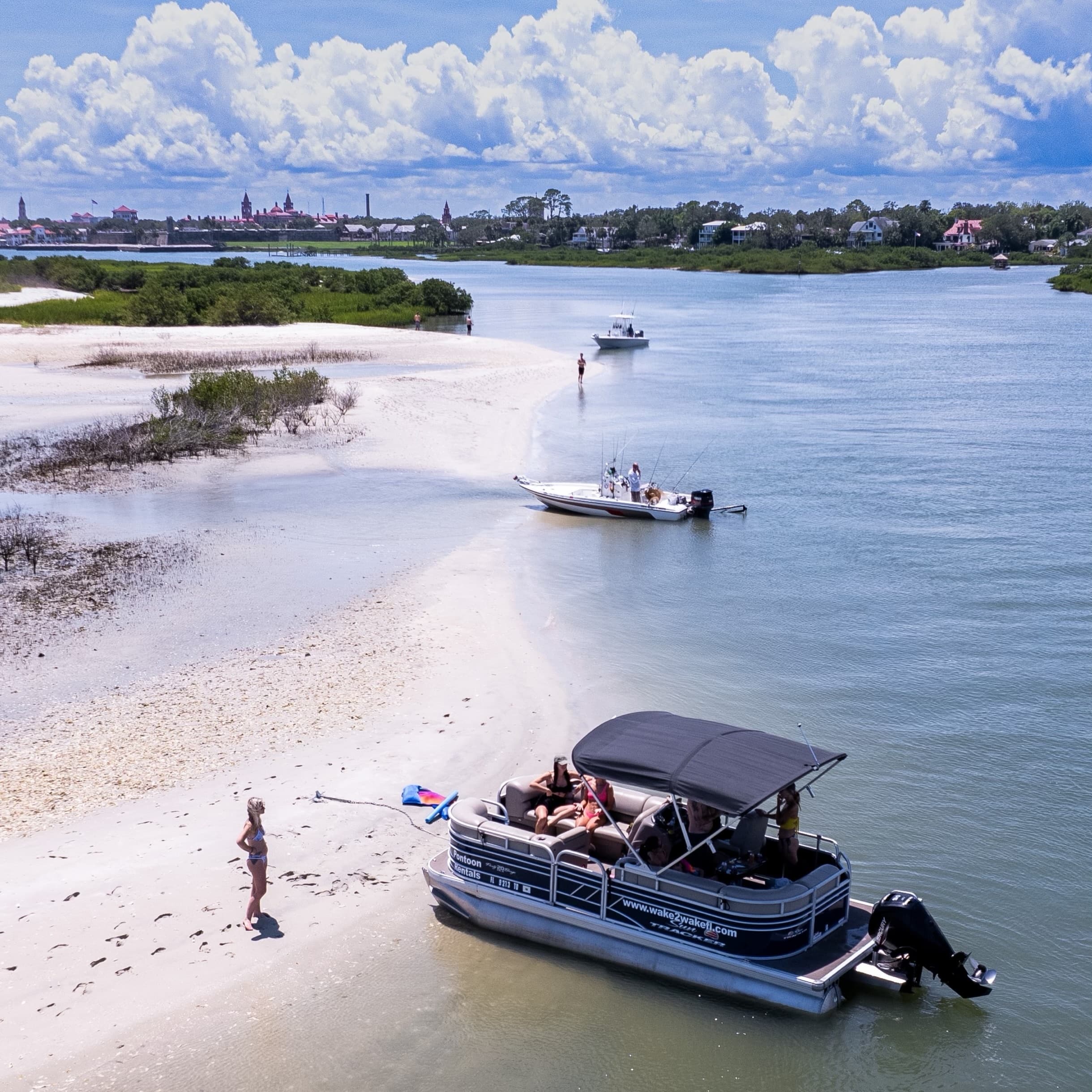 Pontoon boat anchored at sandbar with people enjoying beach
