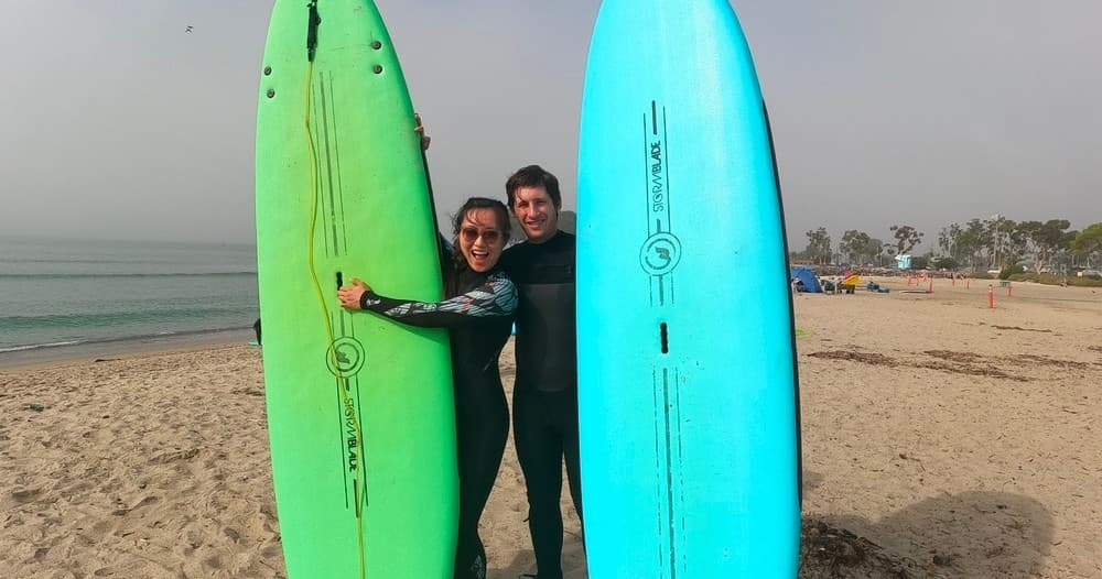 Two surfers posing with green and blue boards on foggy beach