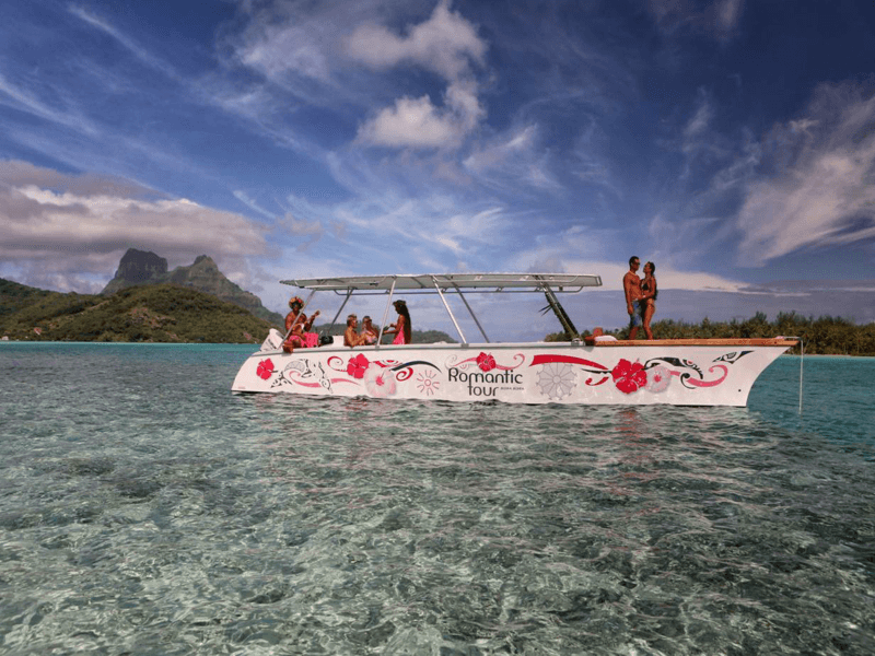 Catamaran anchored on shallow coral reef with mountain backdrop