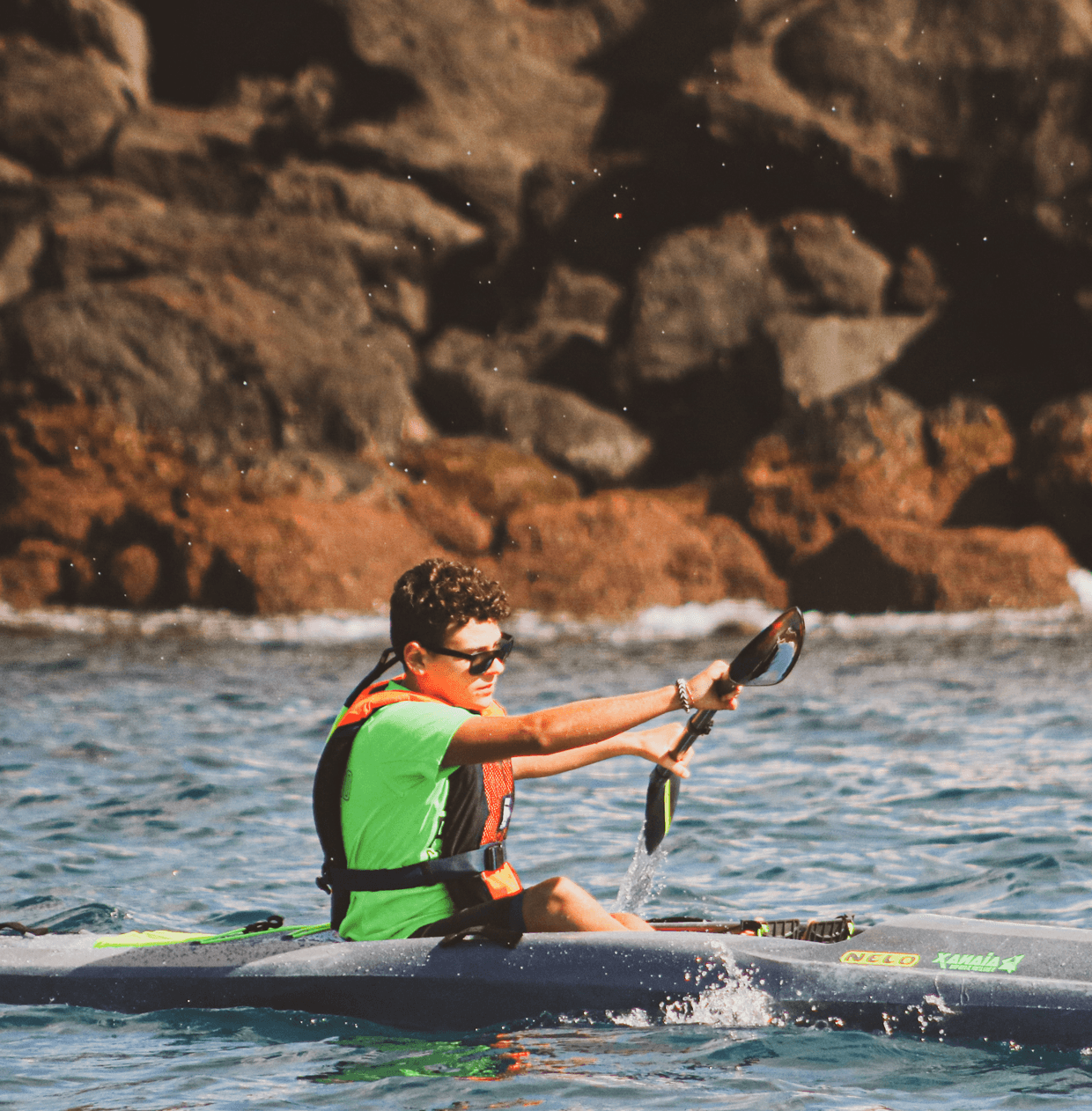 Solo kayaker paddling near rocky coastal shoreline in ocean