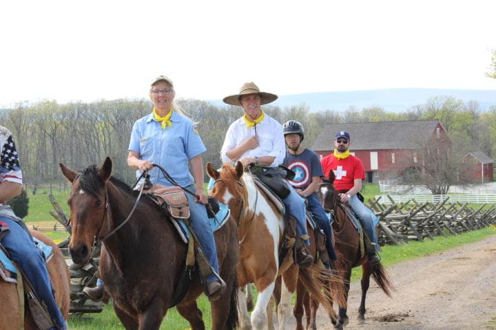 Group horseback riding on scenic farm trail near barn