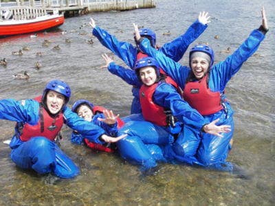 Instructors and teens in wetsuits celebrating in shallow river