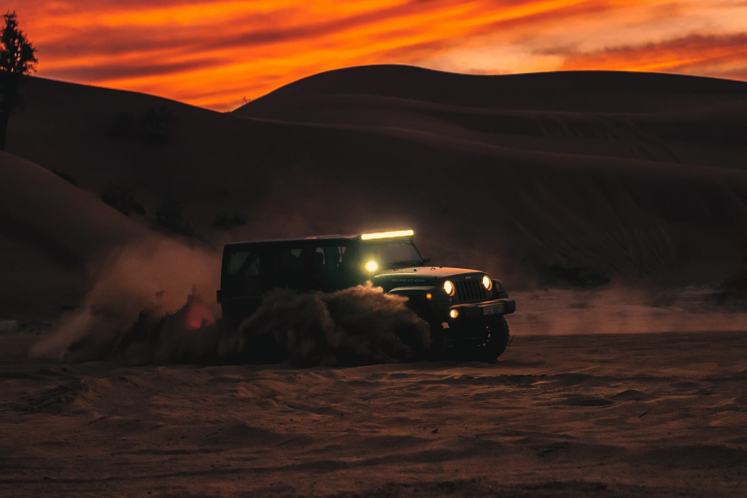 Off-road jeep powering through desert at sunset with headlights