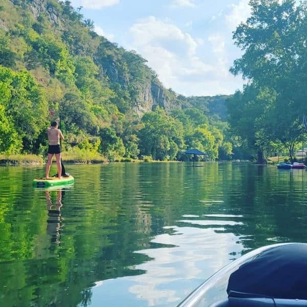 Stand-up paddleboarding on a calm river beside cliffs