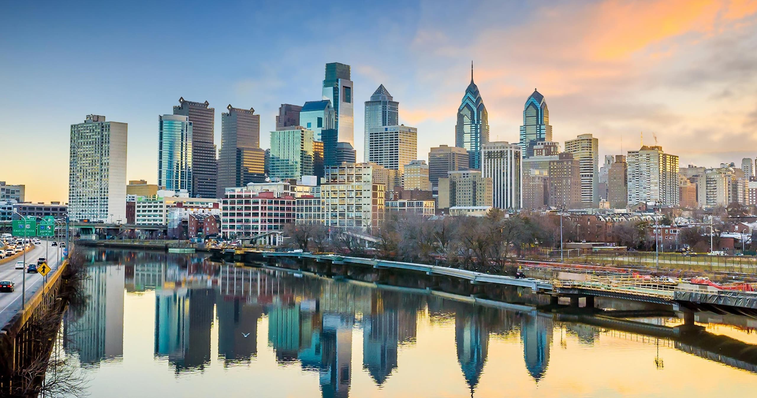 Riverfront city skyline at sunrise with reflective water, urban tour