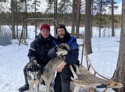 Couple with sled dogs by snowy pine forest, husky sled tour