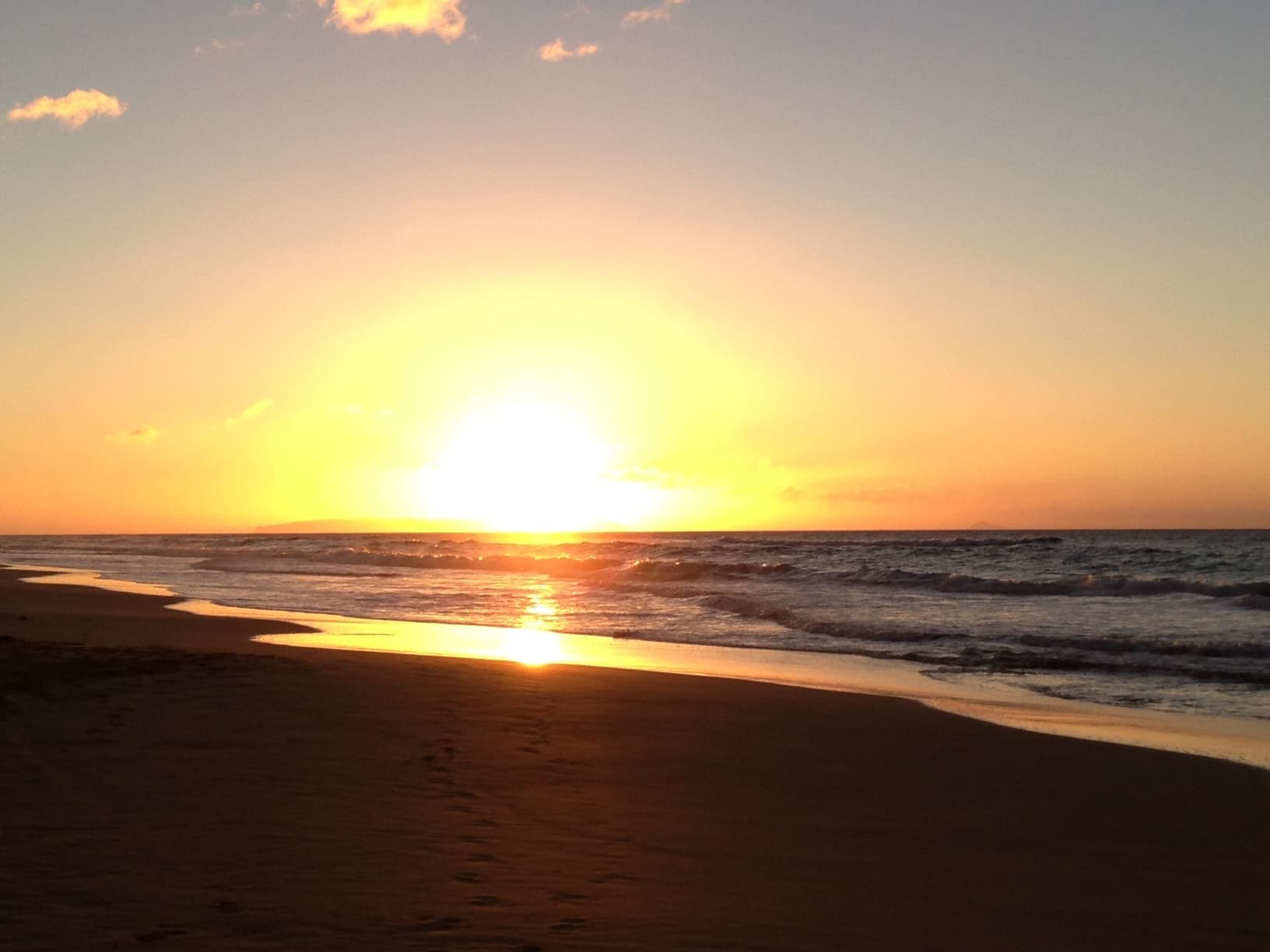 Sunset over Kauai beach casting golden reflection on wet sand