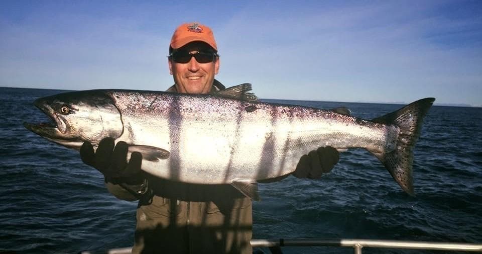 Angler proudly holding large salmon on charter boat at sea