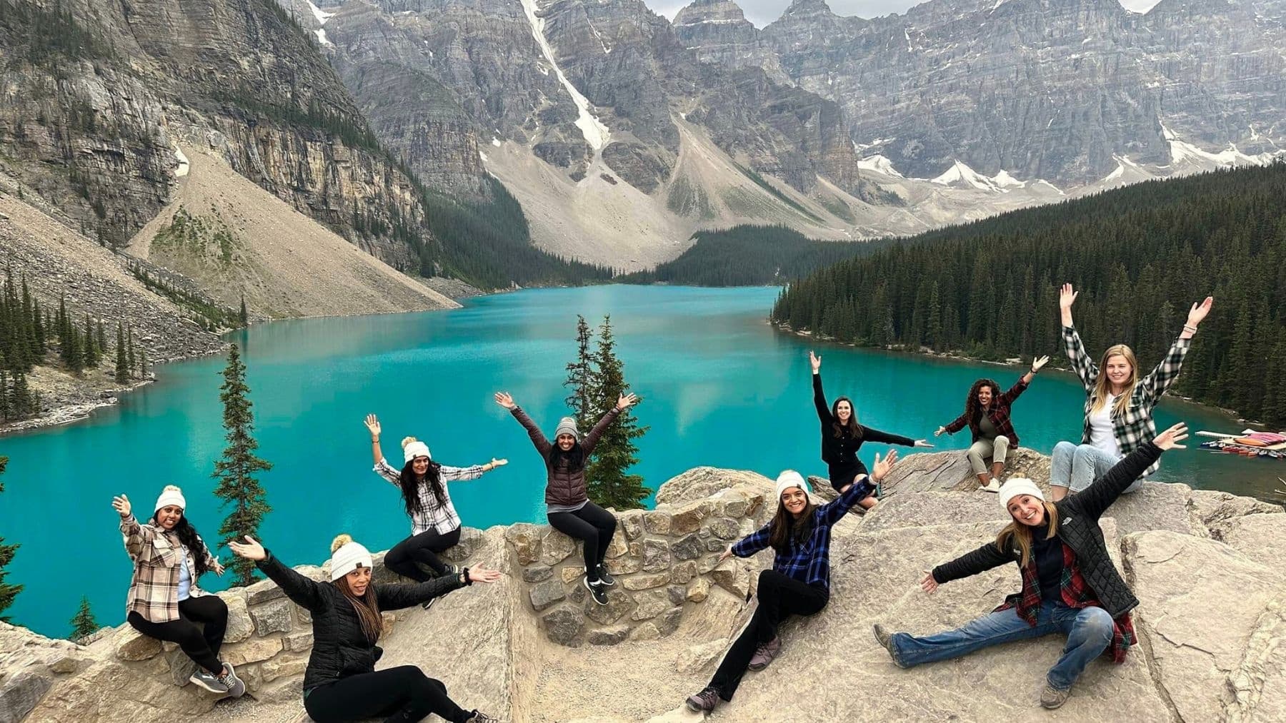 Hikers posing on rocky overlook above turquoise Moraine Lake, Banff