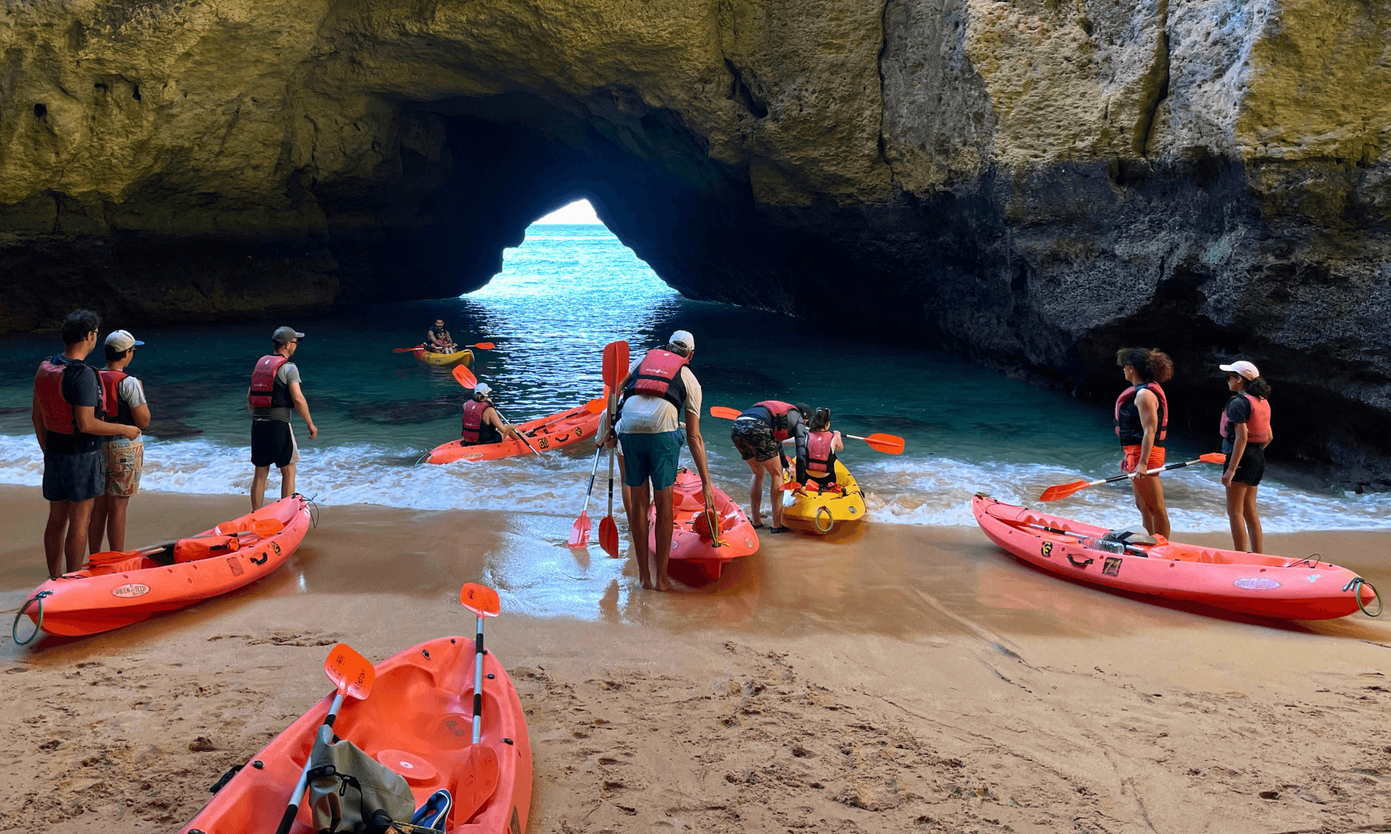 Guided kayak group launching from sandy cave beach on coastal tour