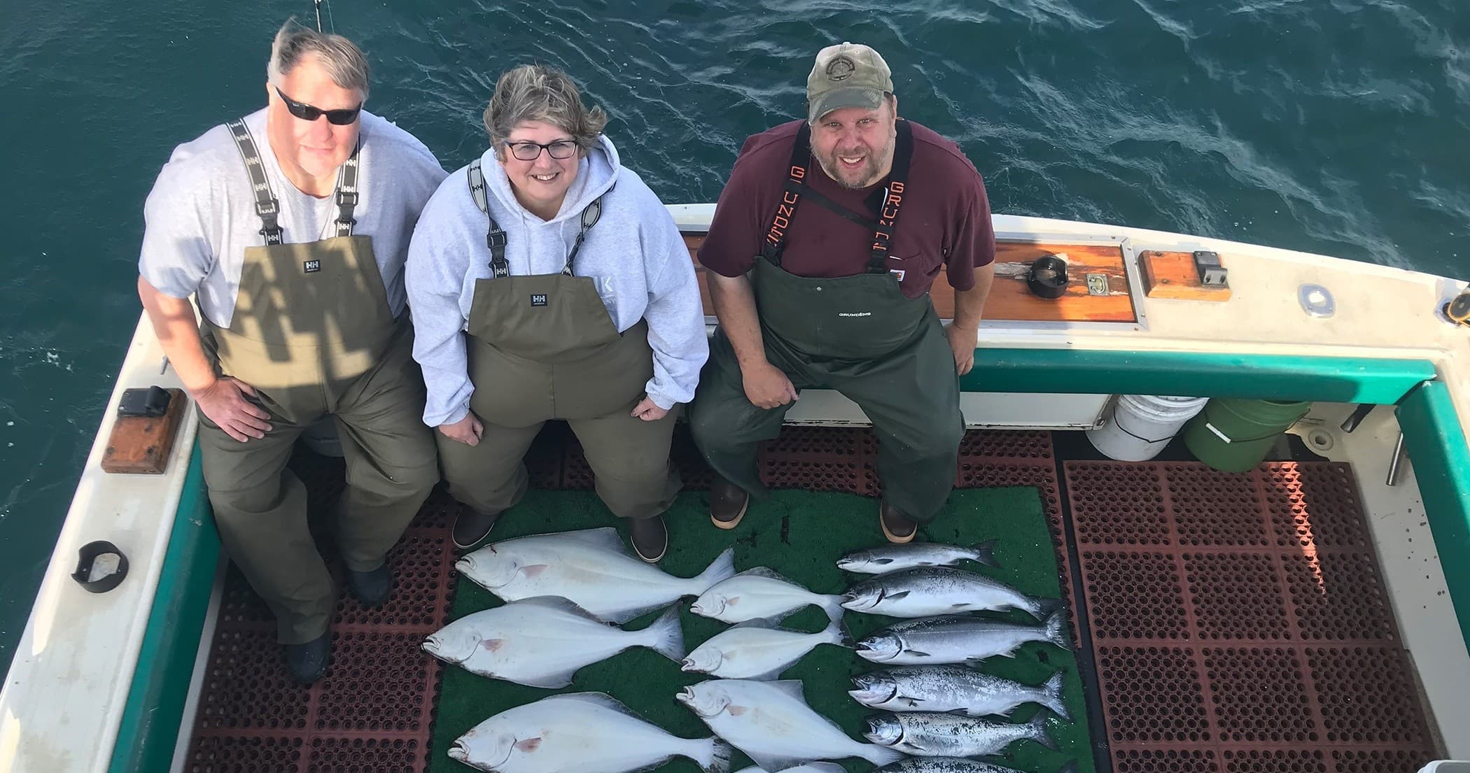 Three anglers posing with halibut and salmon on deck in Alaska
