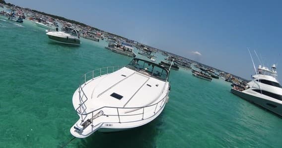 Multiple boats anchored in crowded turquoise sandbar bay, aerial view
