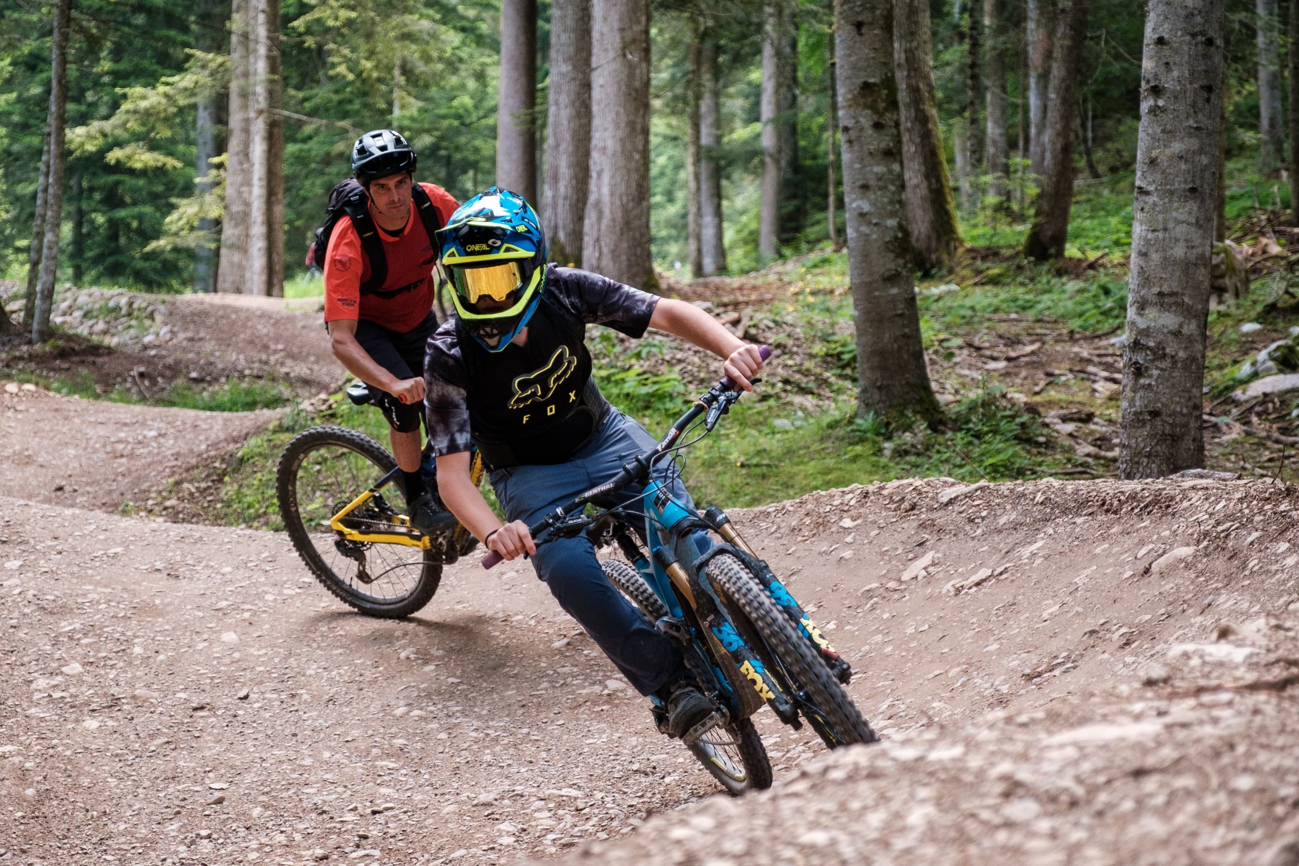 Two mountain bikers leaning through berm on wooded singletrack
