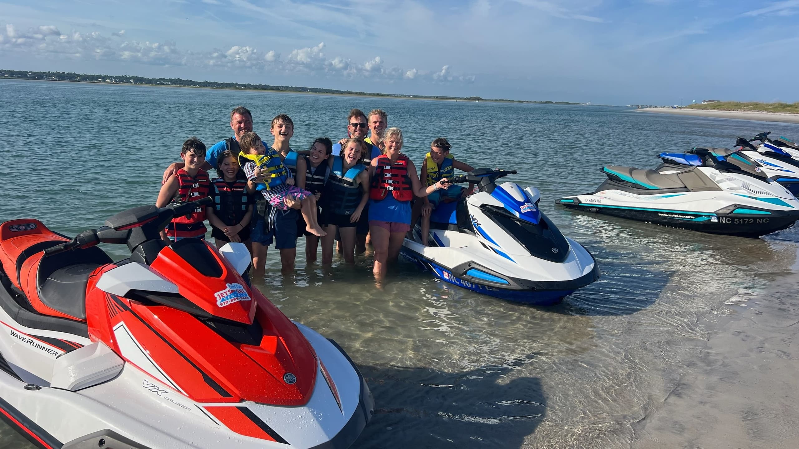 Group posing with colorful jet skis on sandy beach shore