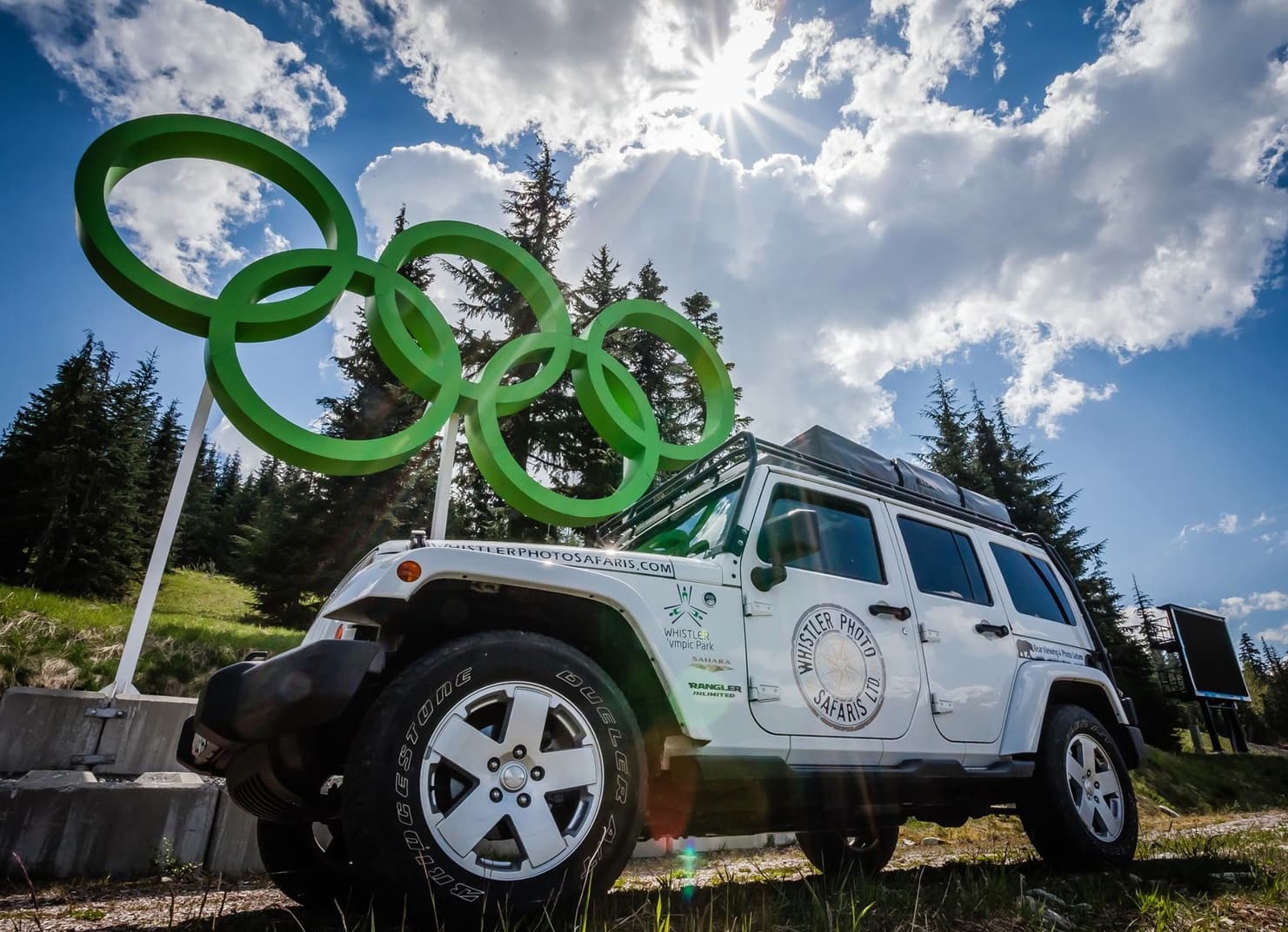 Adventure jeep near Olympic rings sculpture under dramatic sky