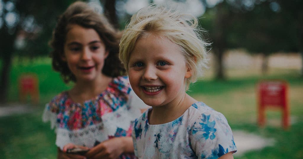 Two young children smiling in grassy park enjoying play