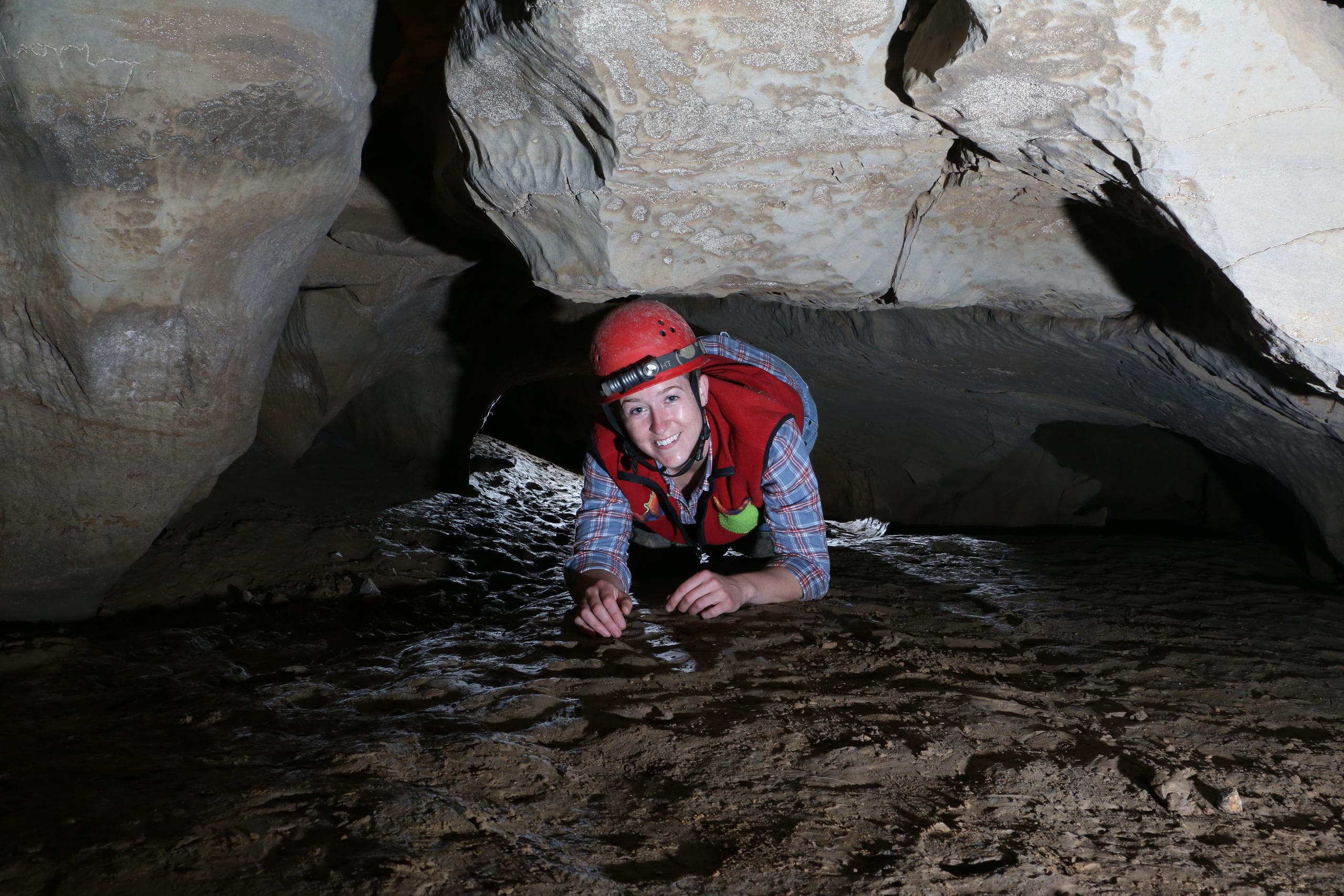 Caver crawling through low limestone tunnel in cave tour