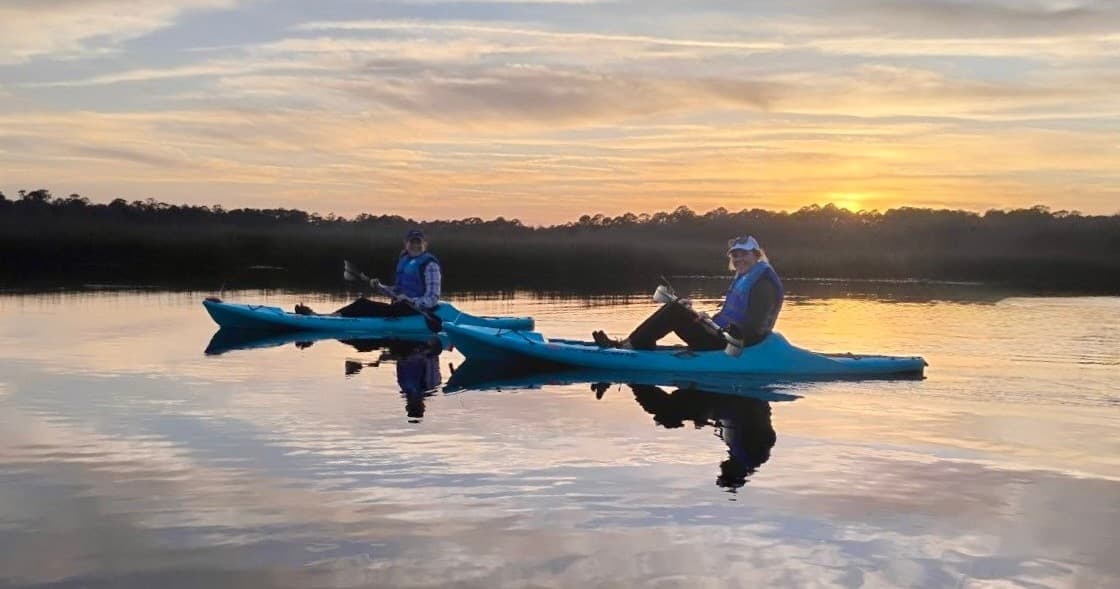 Two kayakers paddling at sunset on calm reflective estuary