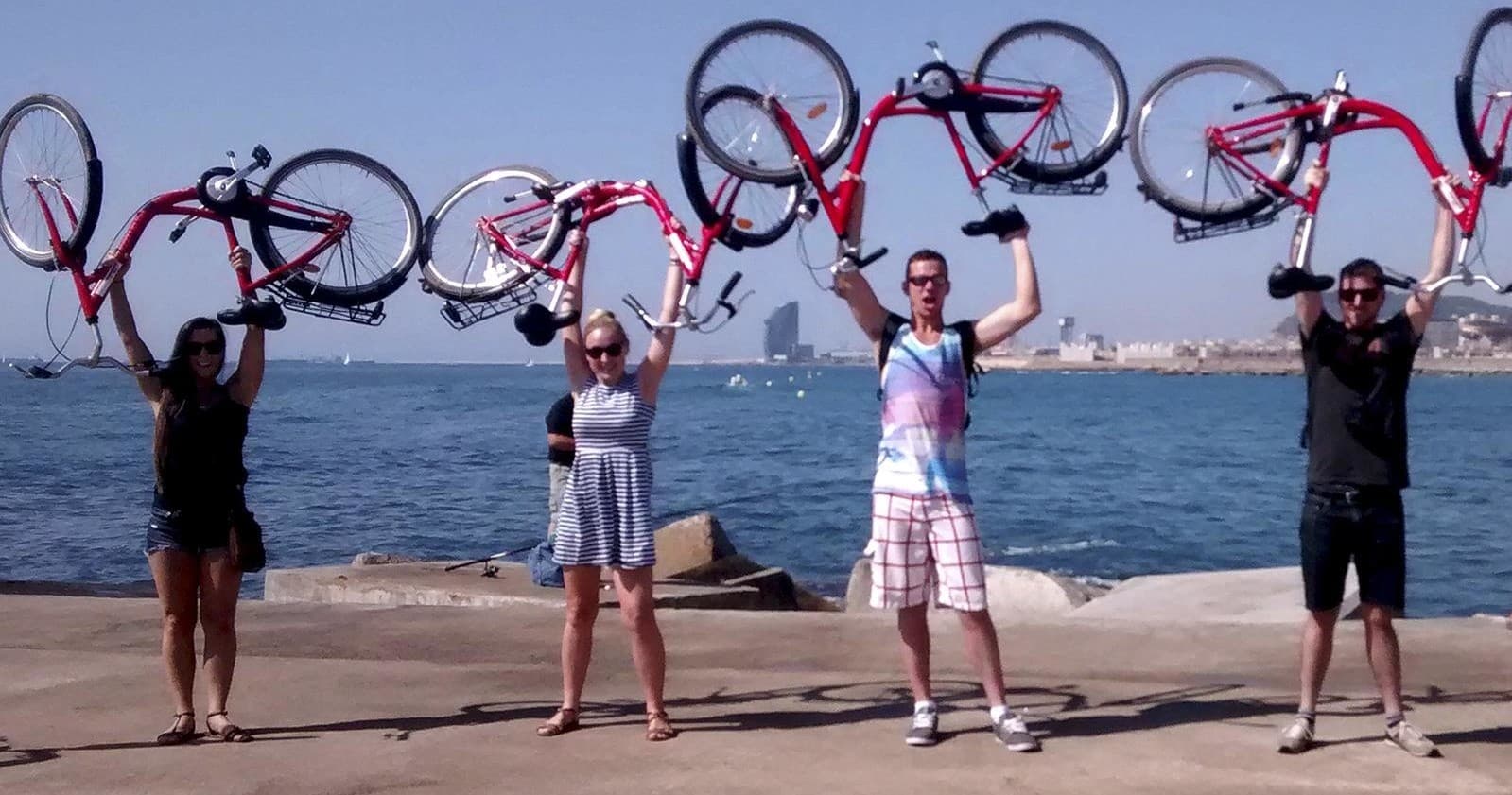 Cyclists lifting bikes by Barcelona waterfront during tour