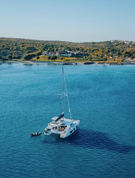 Catamaran anchored in turquoise bay, aerial coastal cruise scene