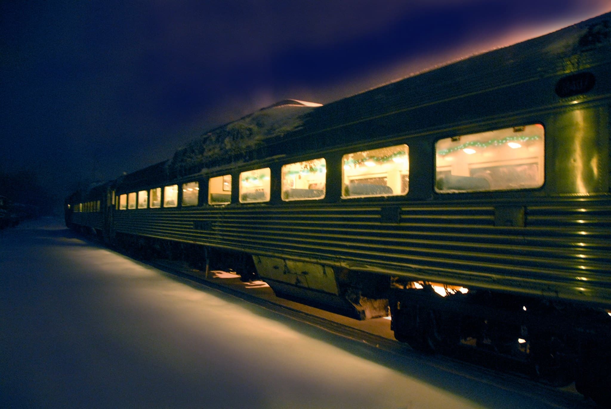 Long vintage railcar lit at night parked along snowy platform