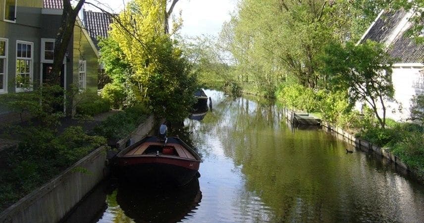 Small boat on quiet tree-lined Amsterdam canal, serene cruise