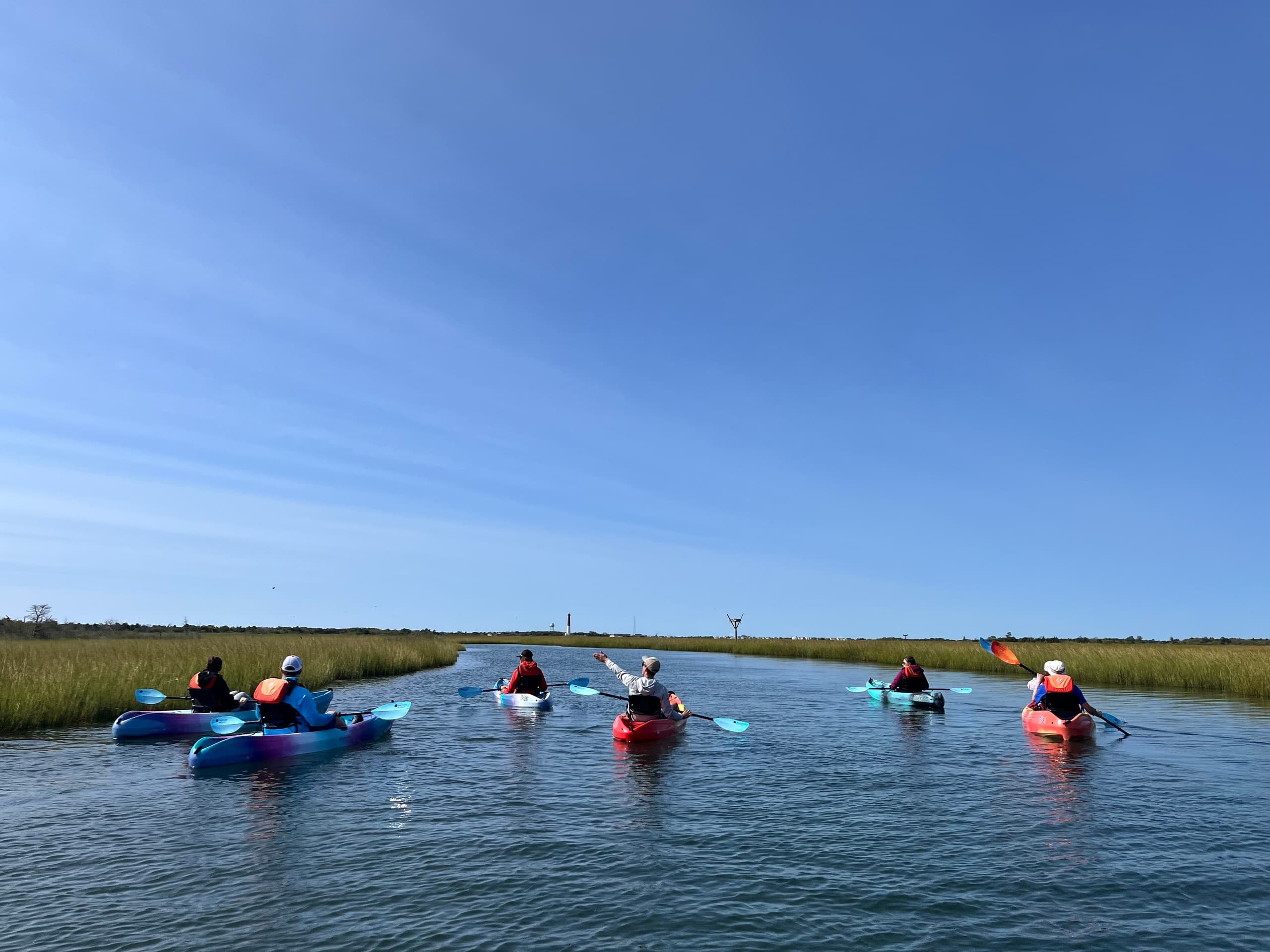 Kayakers paddling through tidal marsh under blue sky