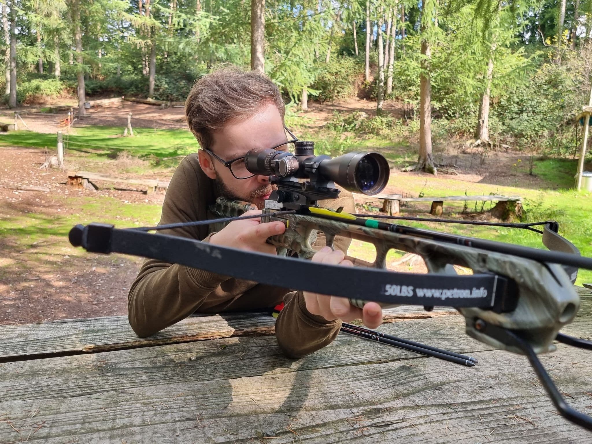 Marksman aiming rifle prone at wooded outdoor shooting range