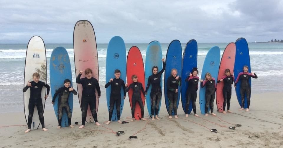 Surf instructors and students lined with colorful surfboards on beach