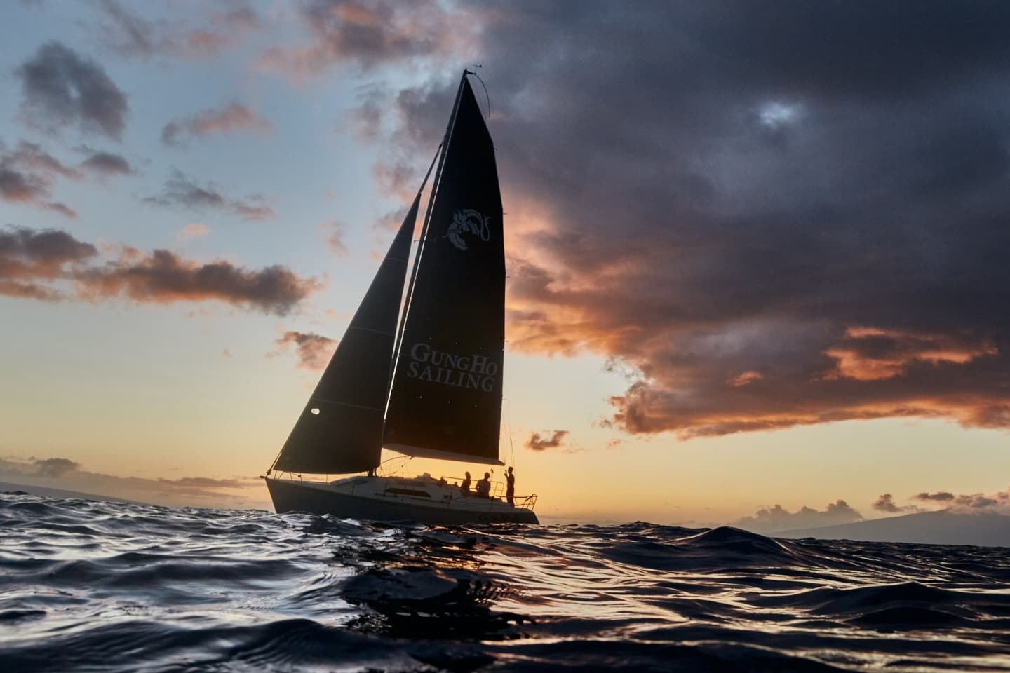 Sailboat silhouette at sunset on open sea with dramatic clouds
